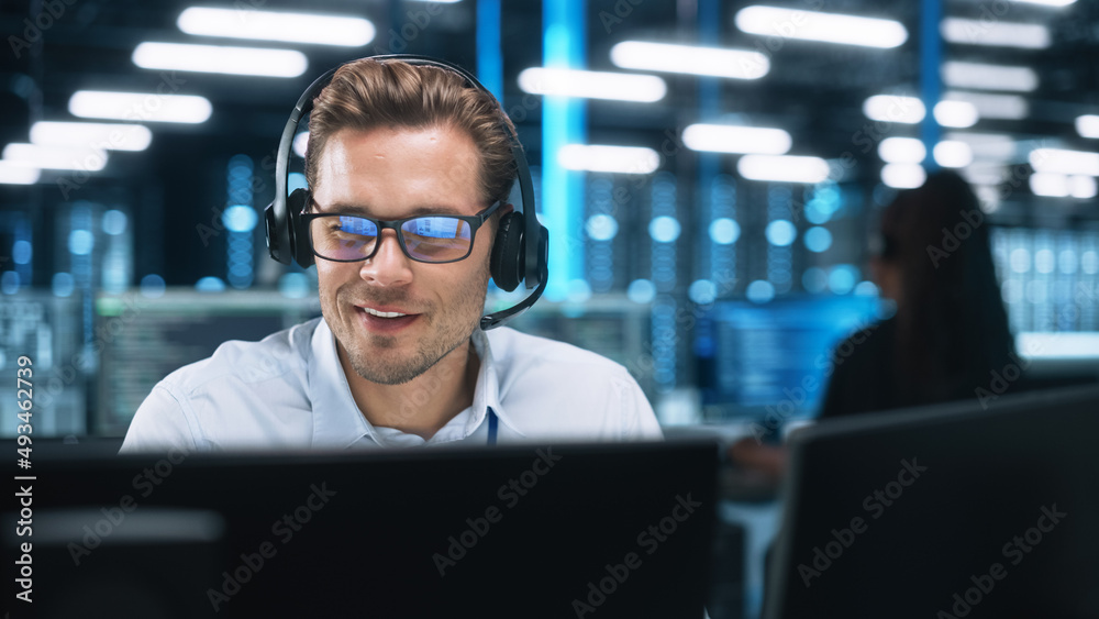 戴着耳机的严肃的年轻高加索男子，呼叫中心的成功经理坐在办公室里，使用Com
