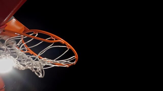 A low angle close-up side view of a basketball net and rim against a black background and arena light, as a free throw is nothing but net for the score.