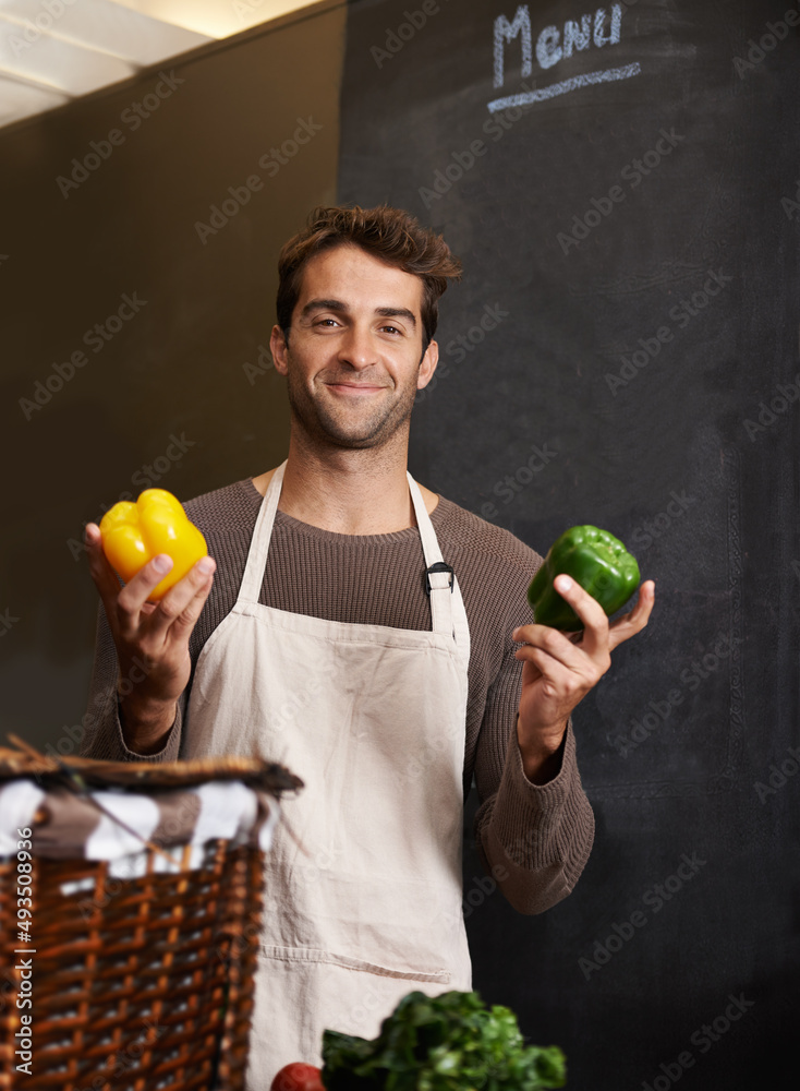 任你选择。一个年轻人在厨房里拿着一个黄绿色的辣椒。