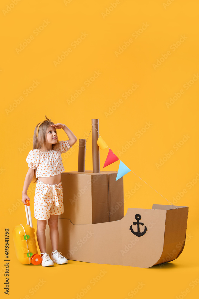 可爱的小女孩在黄色背景下玩纸板船