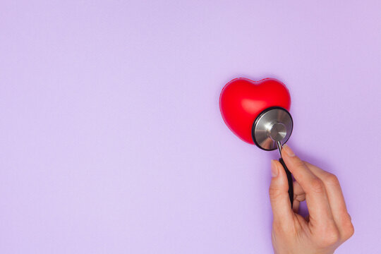 Woman doctor listens to work heart with stethoscope on purple background, flat lay.