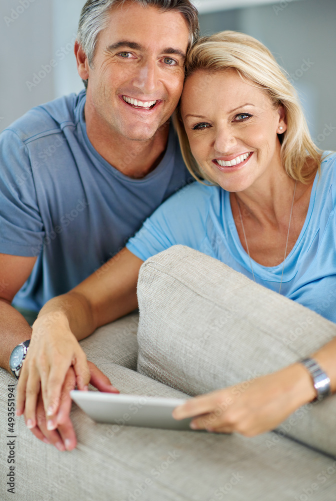 我们是一对现代夫妇。一对微笑的夫妇坐在家里使用数字平板电脑的肖像。