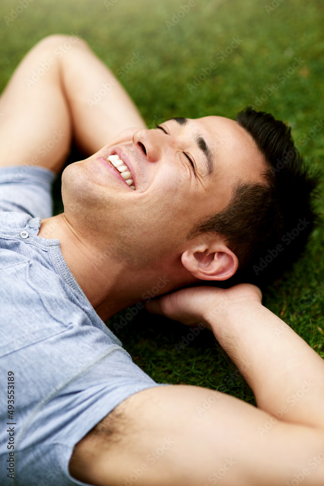 户外给人一种耳目一新的平静感。一个英俊的年轻人在草地上放松的镜头。