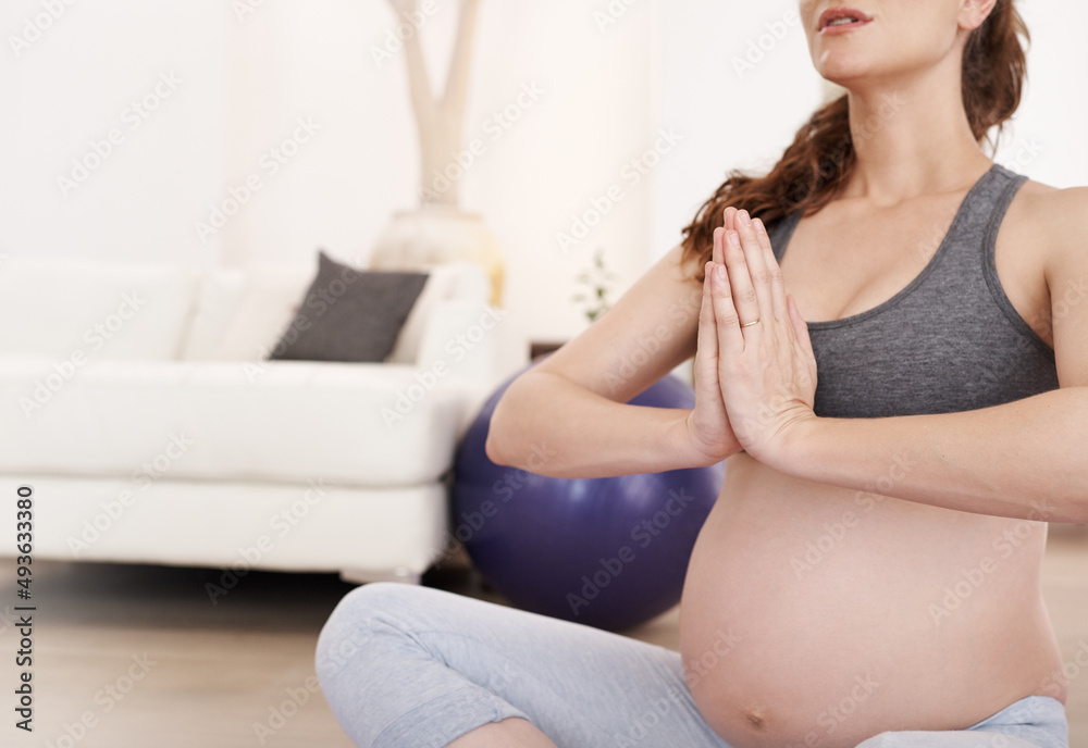 寻找平衡。一个孕妇在家冥想的裁剪镜头。