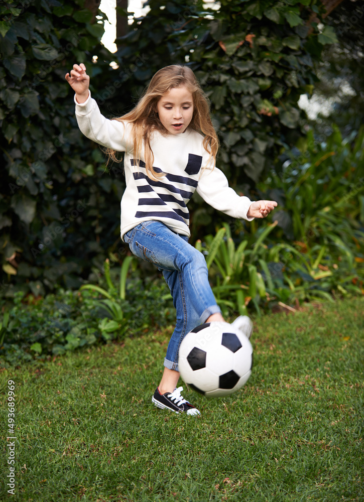 她有点技巧。一个小女孩在花园里玩足球的镜头。