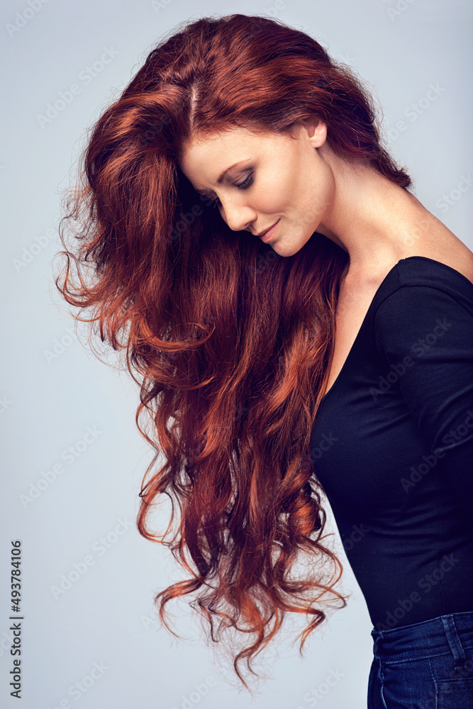 Go on, let your hair down. Studio shot of a young woman with beautiful red hair posing against a gra
