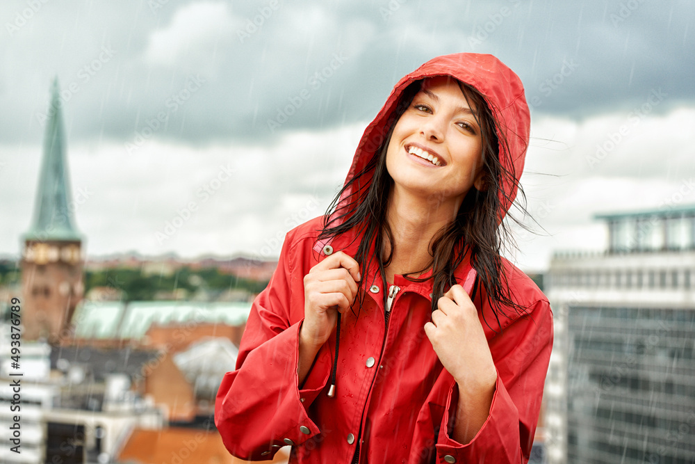雨天不能让她失望。漂亮的年轻女人穿着红色雨衣微笑——肖像。