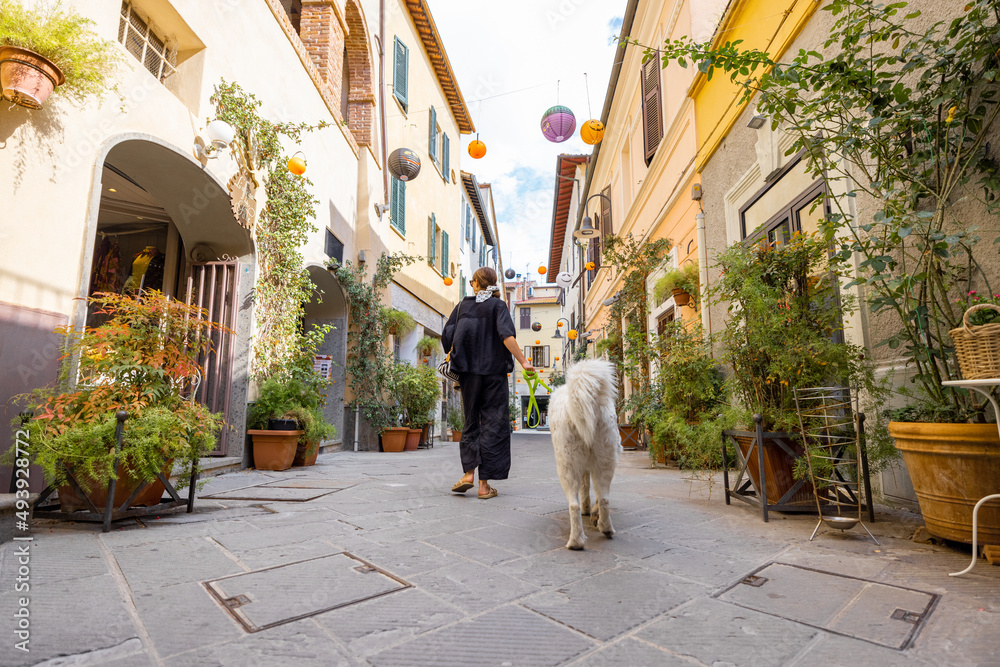 Woman walking with dog on narrow street in the old town of Grosseto, in Maremma region of Italy. Mar