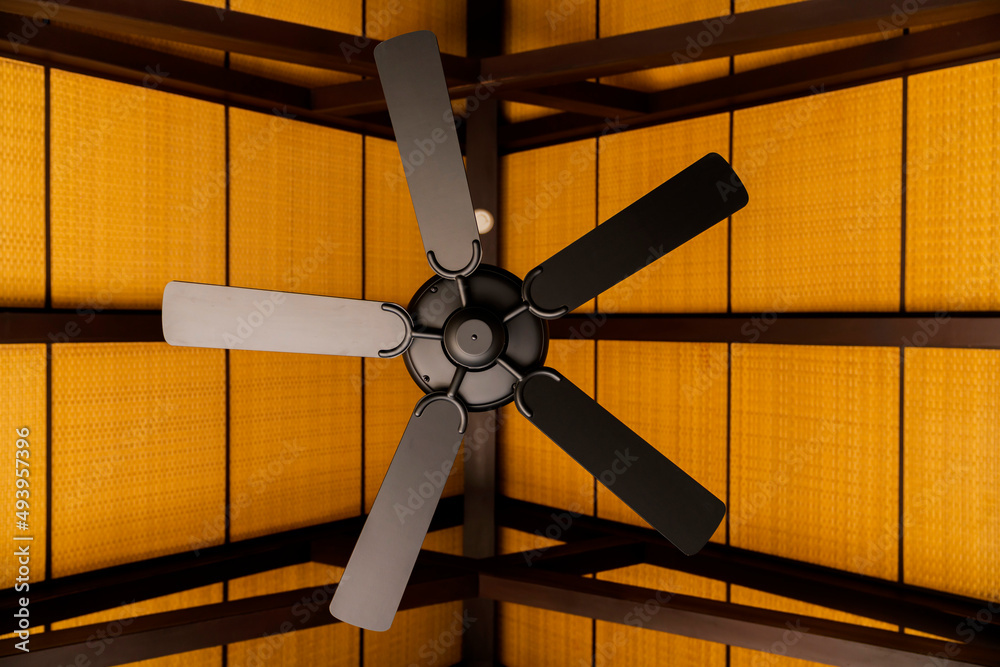 brown indoor ceiling fan on an exposed wooden support beam, with a decorate wooden ceiling, in the h