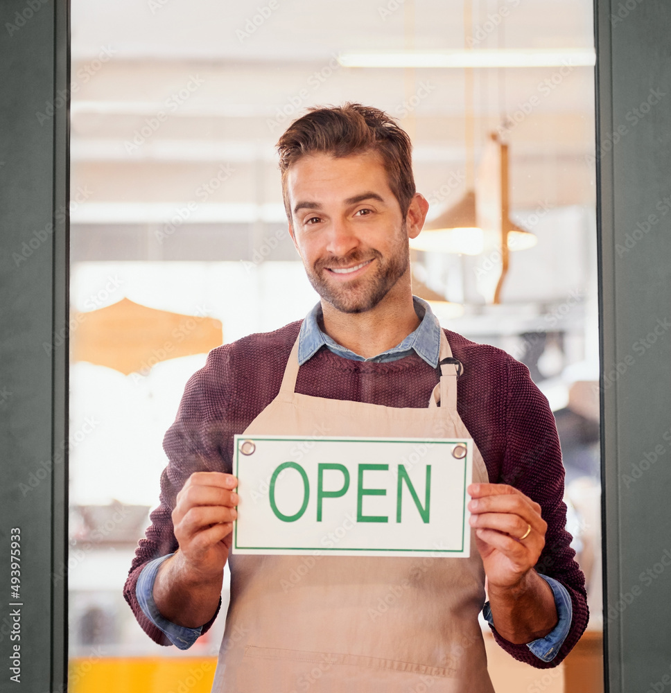 进来吧。一位年轻的企业主站在他的咖啡店门口的照片。