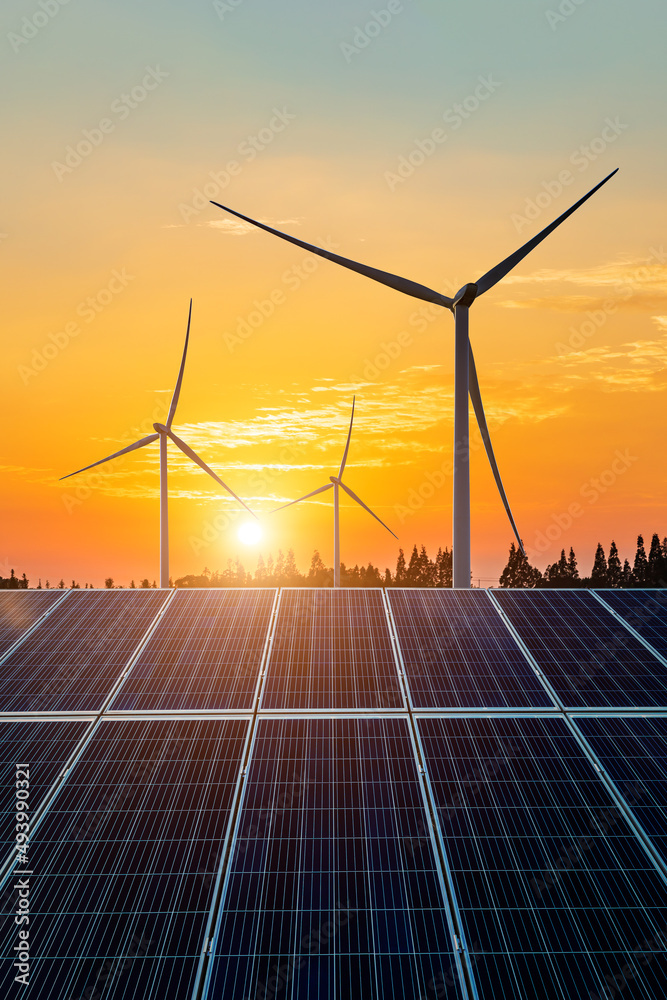 日落时的风力涡轮机和太阳能电池板。可再生能源概念。