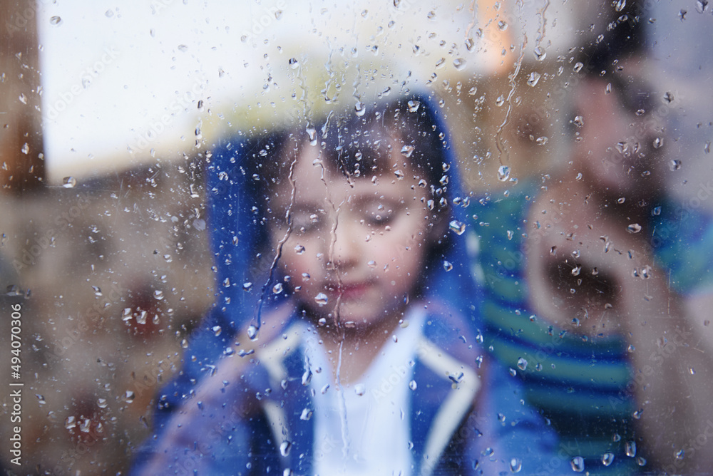 雨天无所事事……一个小男孩在一扇布满雨水条纹的窗户后面向下看。