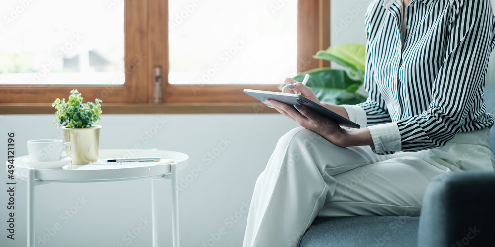 女人坐在家里的沙发上享受数字平板电脑上的内容社交媒体应用。