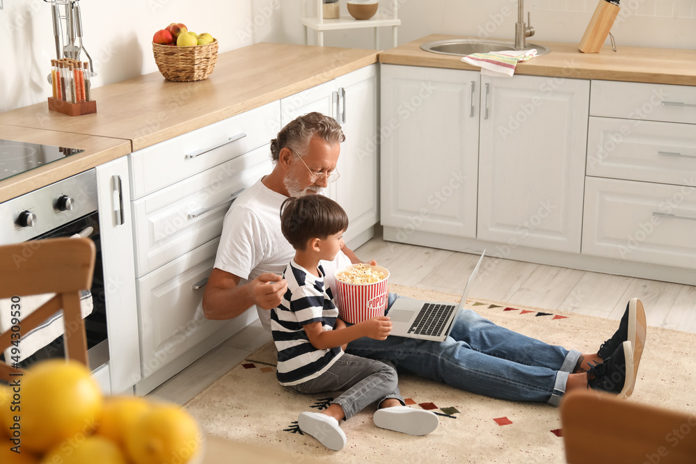 小男孩和他的爷爷在厨房里用笔记本电脑吃美味的爆米花