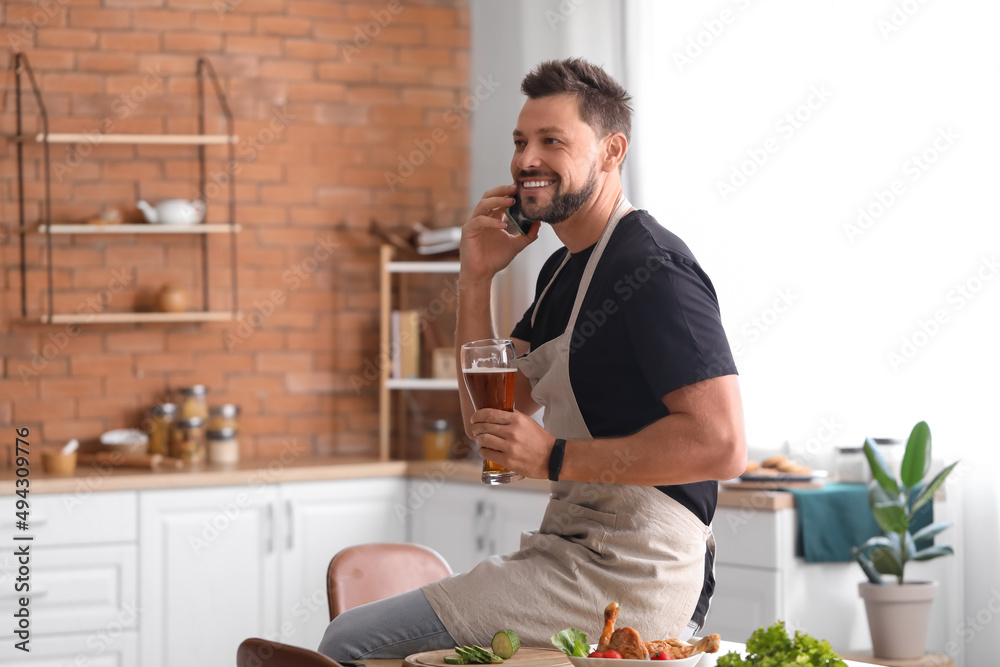 英俊的男人在厨房打电话时喝啤酒