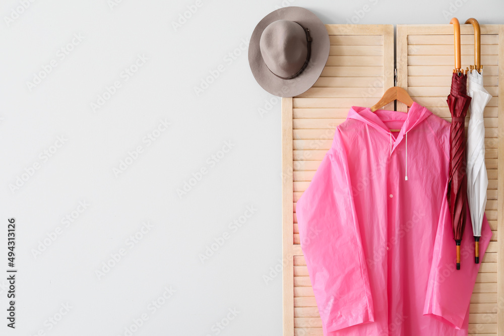 带粉色雨衣、雨伞和帽子的折叠屏幕靠近灯光墙