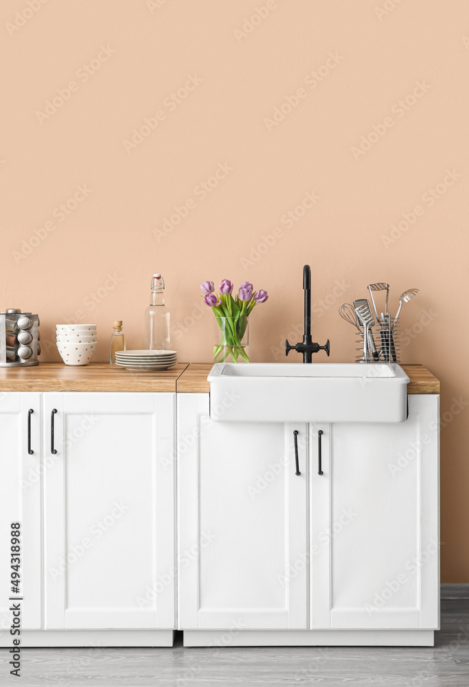 白色柜台，带水槽，花瓶中的郁金香和米色墙壁附近的厨房用具