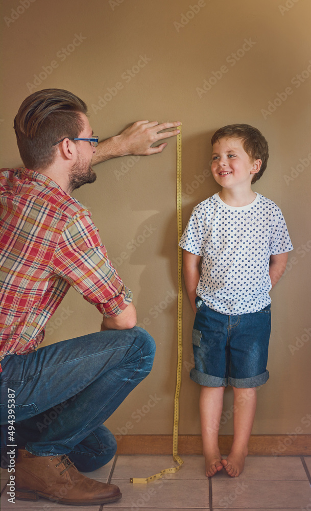 看看你长得多大了。一位父亲在家里靠墙测量孩子身高的照片。