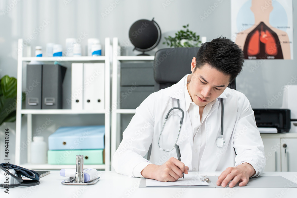 亚洲专科男医生在办公室医院的桌子上写笔记。