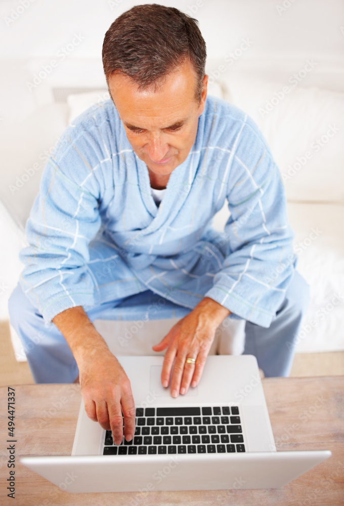 一位穿着浴袍的老人在家里用笔记本电脑工作。一位退休老人工作的仰视图