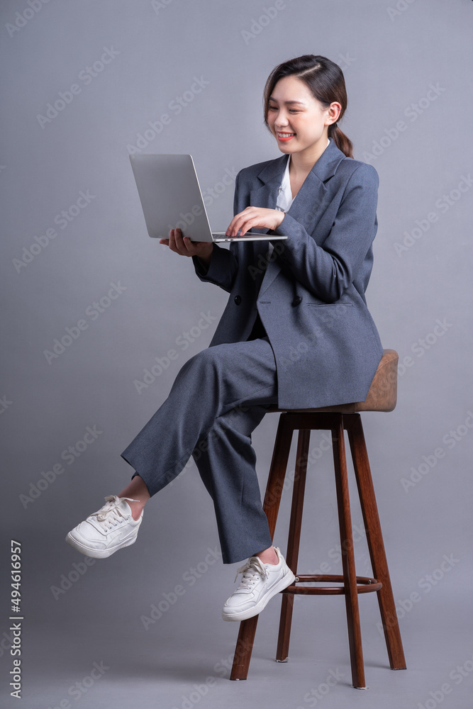年轻的亚洲女商人坐在椅子上，用灰色背景的笔记本电脑