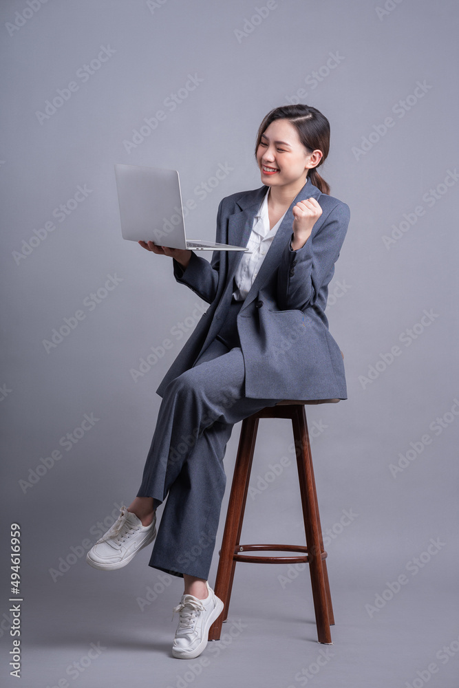年轻的亚洲女商人坐在椅子上，用灰色背景的笔记本电脑