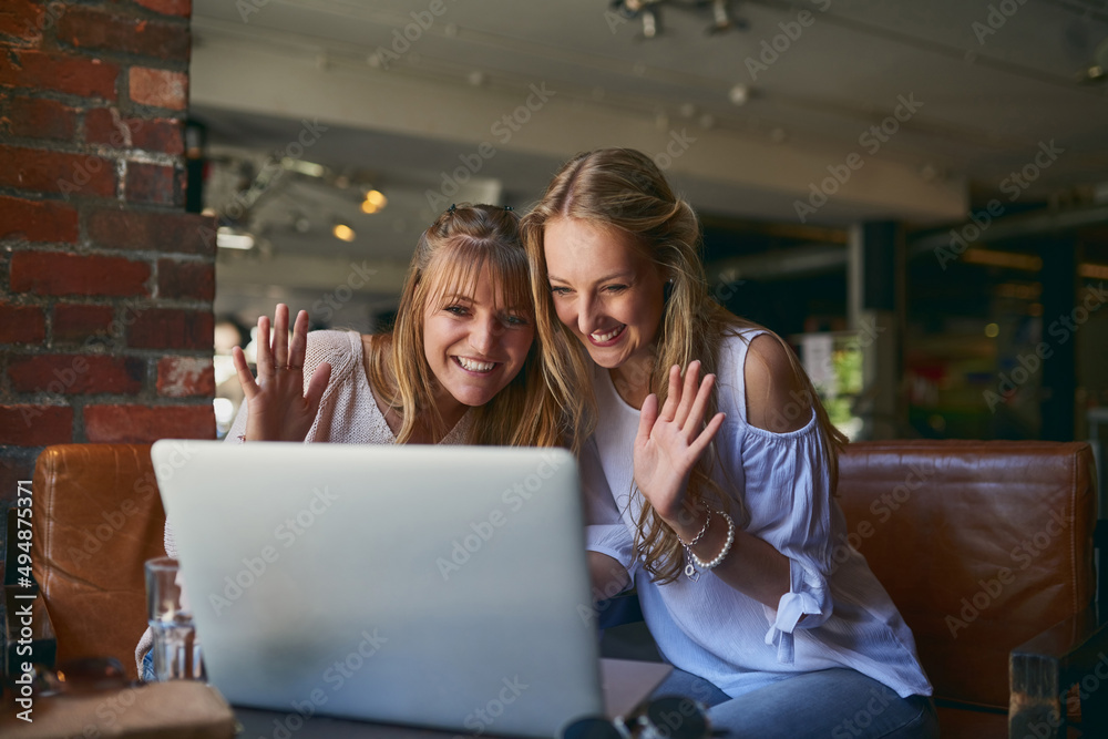 你好。两个漂亮的年轻女友坐在一个房间里通过笔记本电脑视频聊天的裁剪镜头