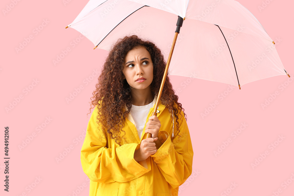 忧心忡忡的年轻非裔美国妇女穿着黄色雨衣，粉色背景带伞