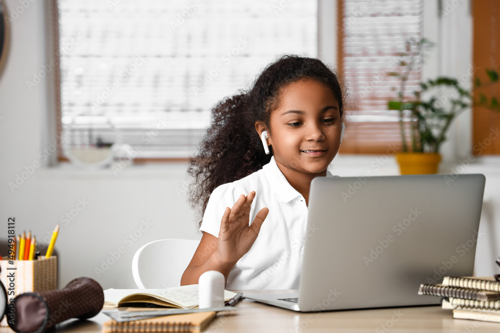 戴着耳机的美国黑人小女孩在家里与在线导师学习
