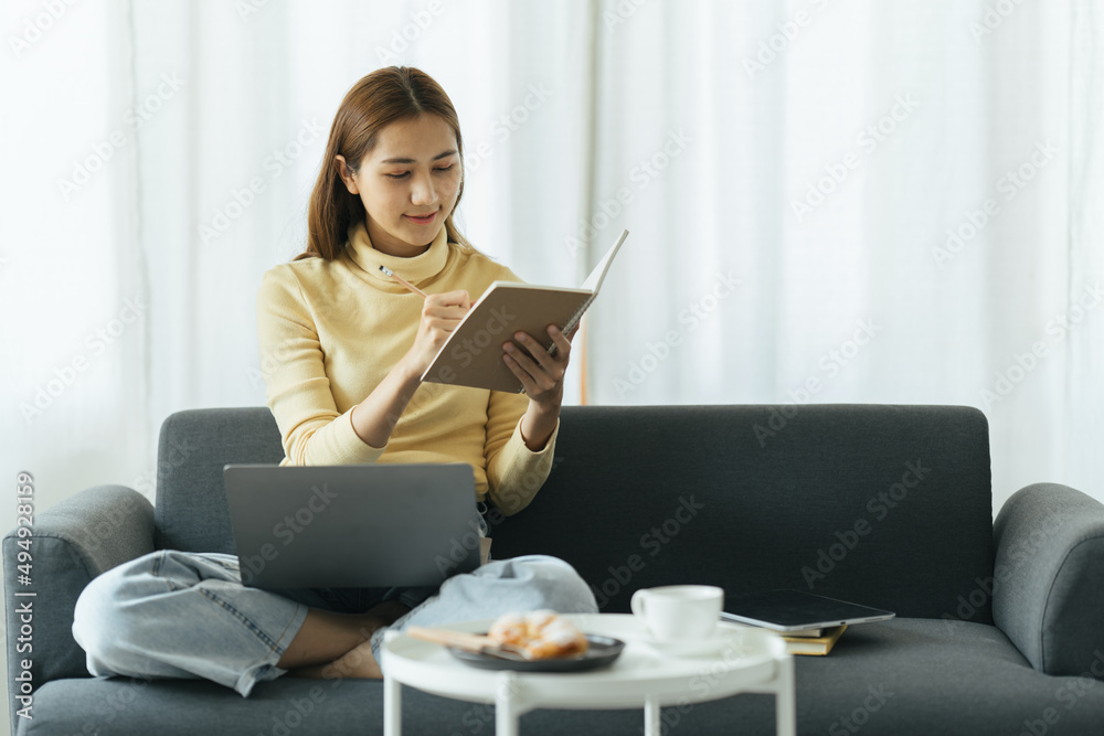 在线教育。年轻的亚洲女孩在家用笔记本电脑学习，边看网络研讨会边做笔记