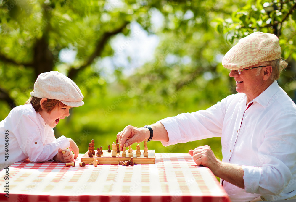 快乐的爷爷和孙子在春天花园下棋