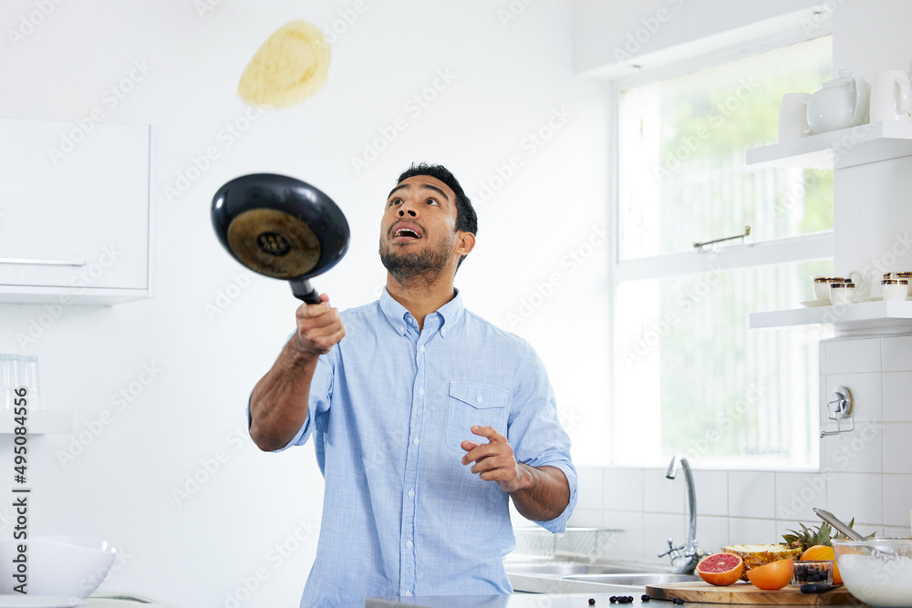 你必须在食物上玩得开心。一个年轻人在家做煎饼的镜头。
