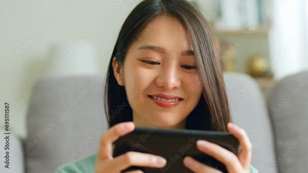 微笑年轻的亚洲女性在家里用智能手机玩游戏和在社交媒体上聊天。