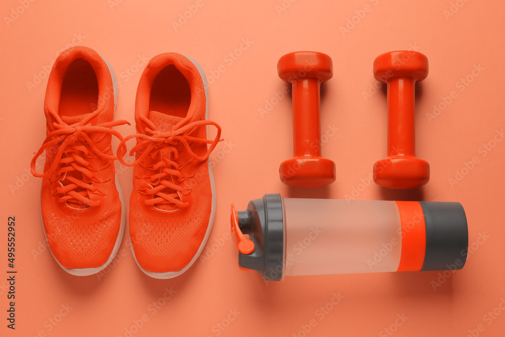 橙色背景的运动鞋、哑铃和一瓶水，俯视图