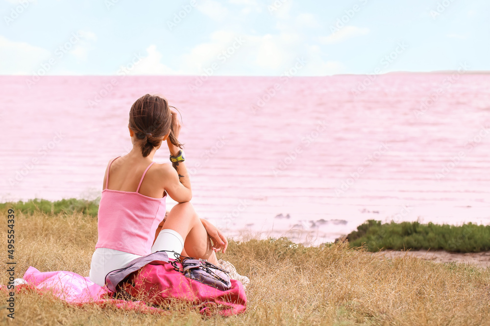 背着背包的年轻游客坐在粉红色的湖边