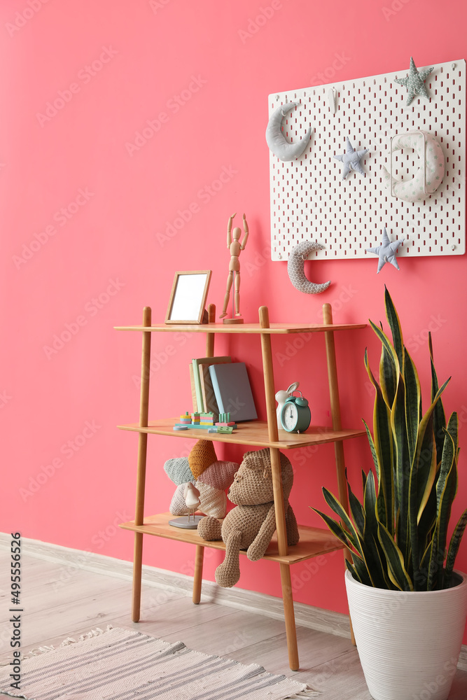 粉色墙上挂着玩具、室内植物和钉板的架子