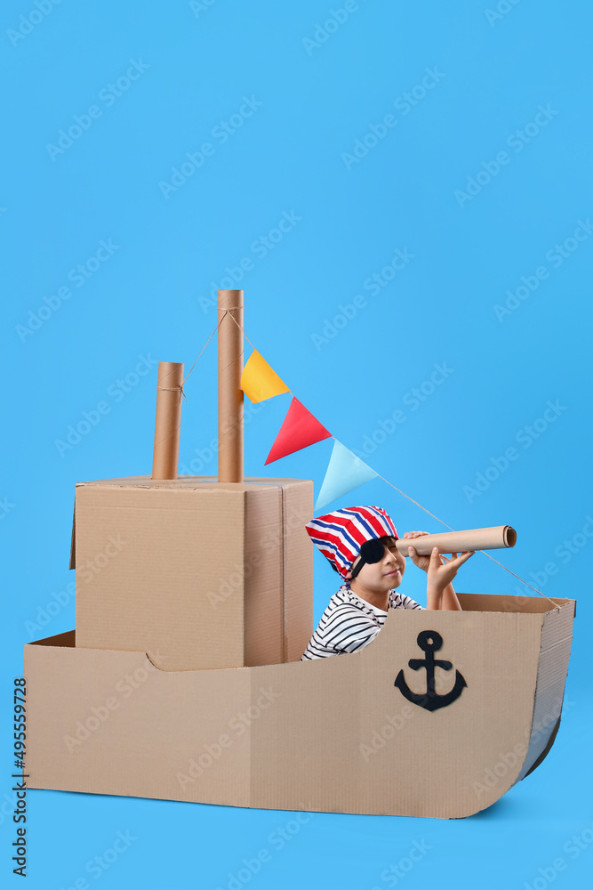 可爱的小男孩在蓝色背景下玩纸板船