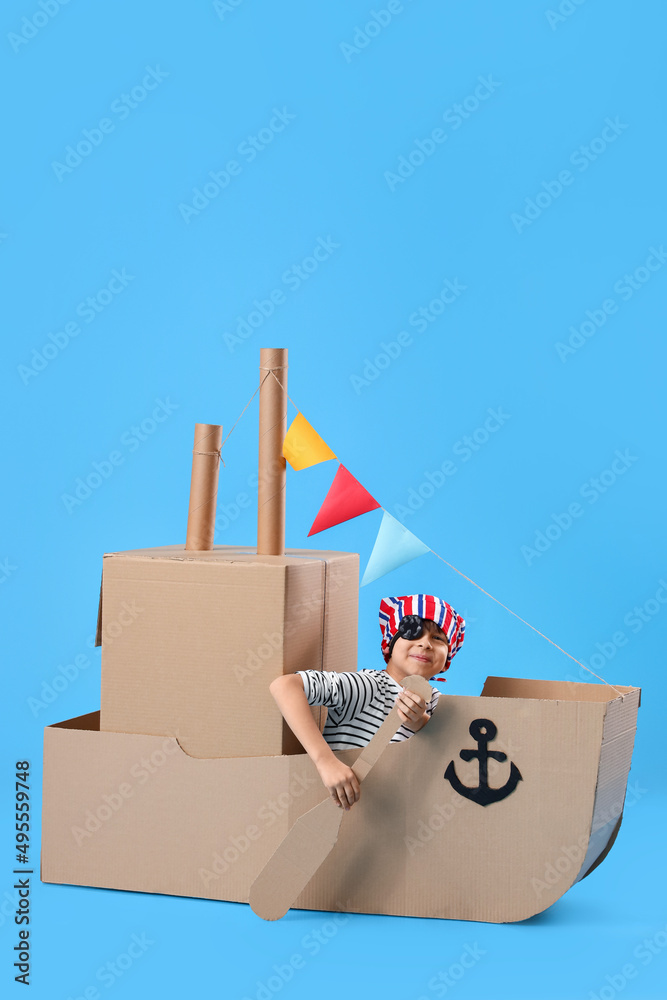 可爱的小男孩在蓝色背景下玩纸板船