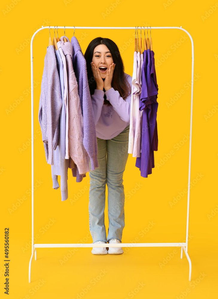 惊讶的年轻亚洲女人和黄色背景紫色衣服的架子