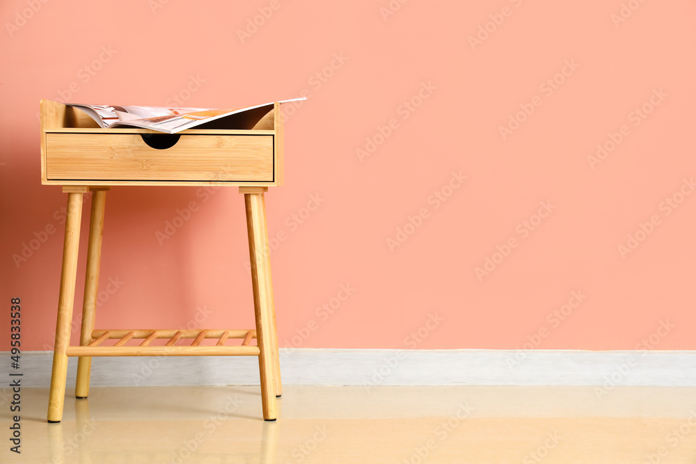 Wooden table with magazine near pink wall