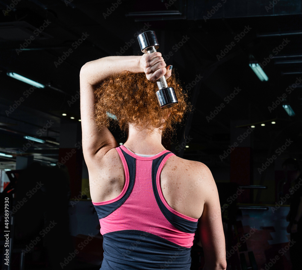 魅力四射的年轻女子在健身房练习哑铃。