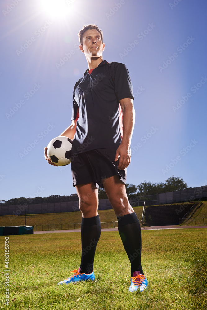 比赛英雄。一张年轻足球运动员站在球场上，手里拿着球的照片。