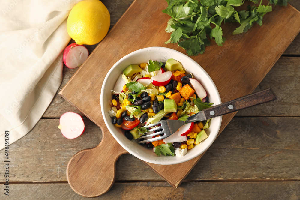 Board with bowl of delicious Mexican vegetable salad on wooden background