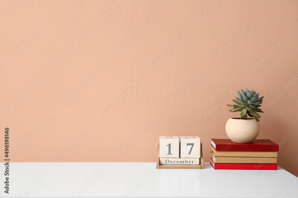 彩色墙附近桌子上的一叠书、室内植物和立方体日历