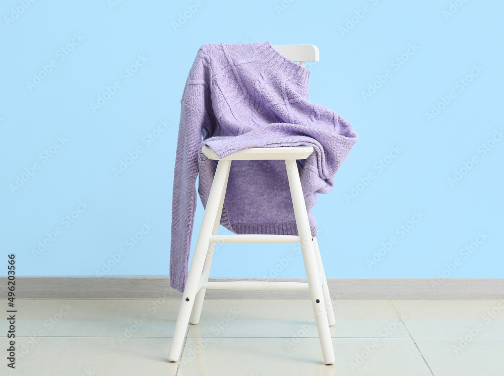 椅子上靠近彩色墙的时尚淡紫色毛衣