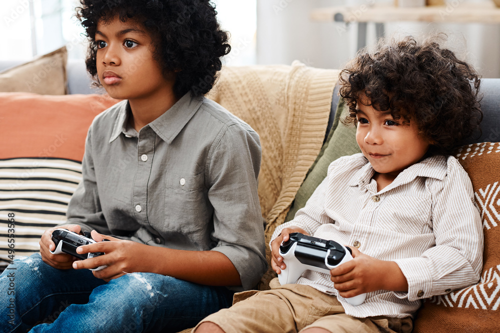 游戏时间到了。两个可爱的小男孩坐在沙发上玩电子游戏的裁剪镜头