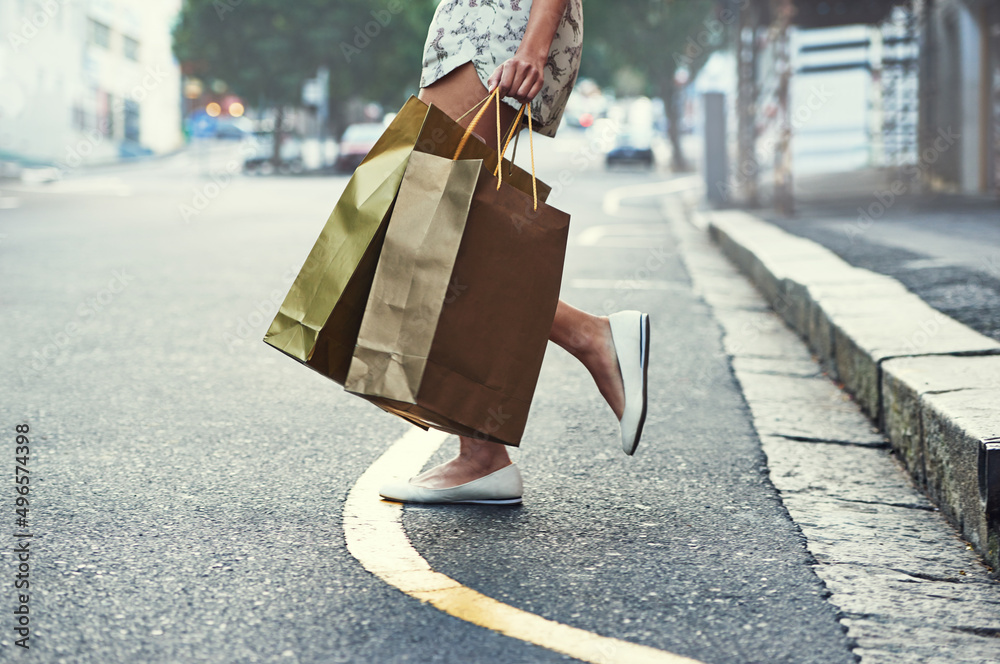 购物是她的有氧运动。一个女人拿着购物袋穿过城市街道的裁剪镜头。