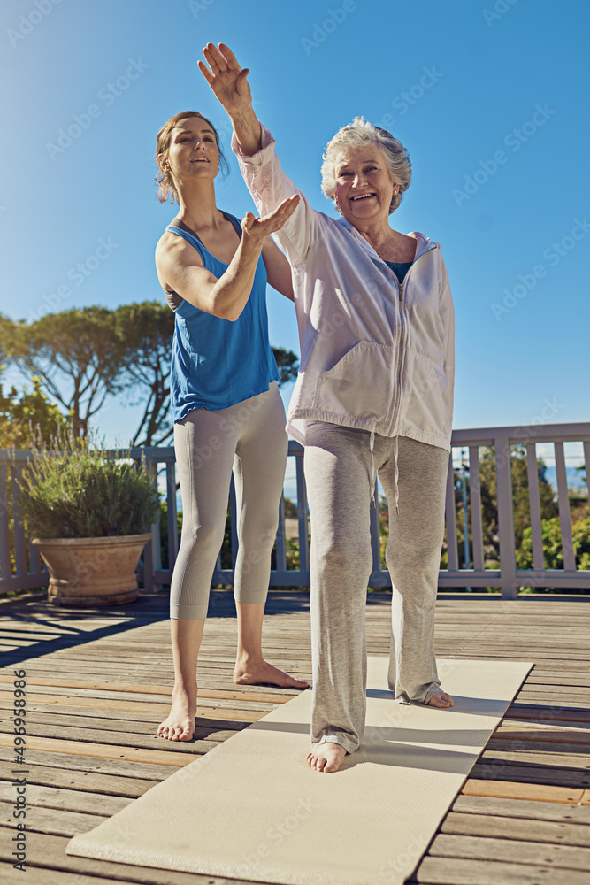 在黄金岁月里改善健康。一位资深女性与教练在露台上做瑜伽的照片