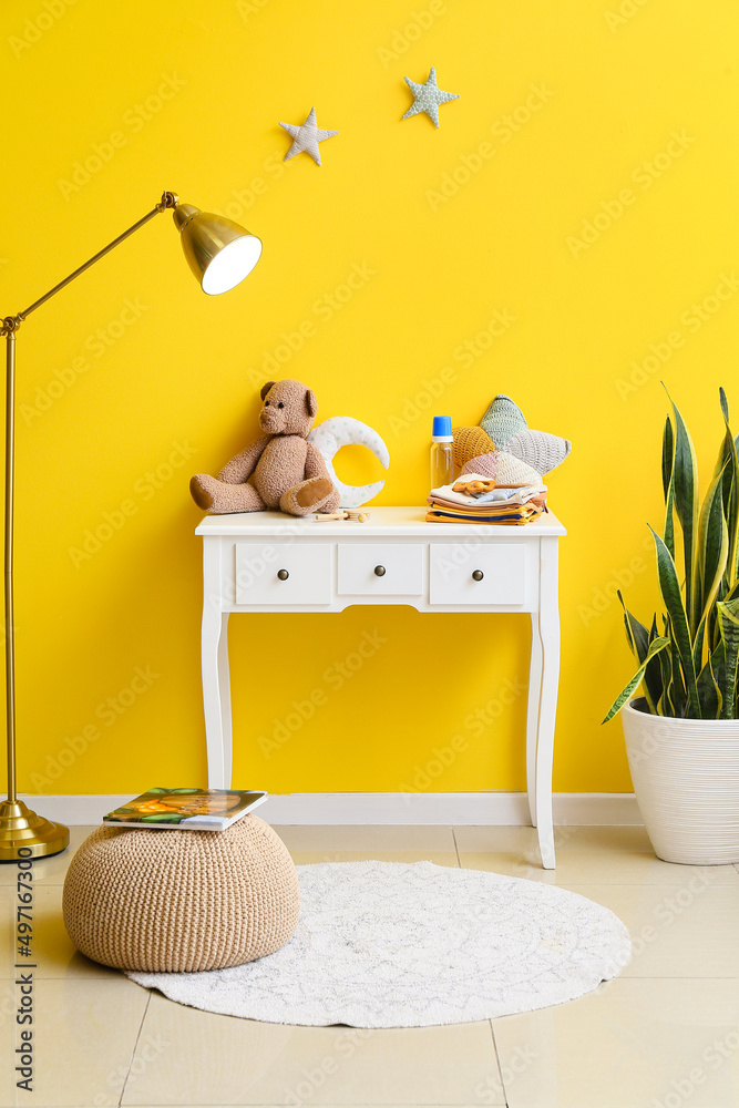 黄色墙壁附近有婴儿衣服、玩具、灯和室内植物的桌子