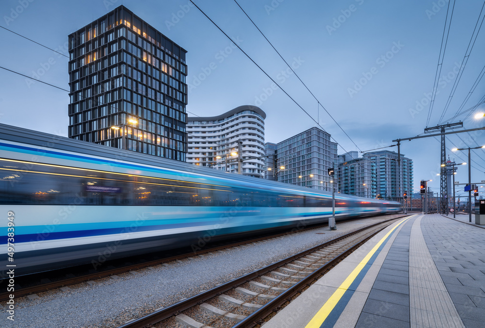 黄昏时分，高速列车在火车站上行驶。蓝色现代城际客运列车
